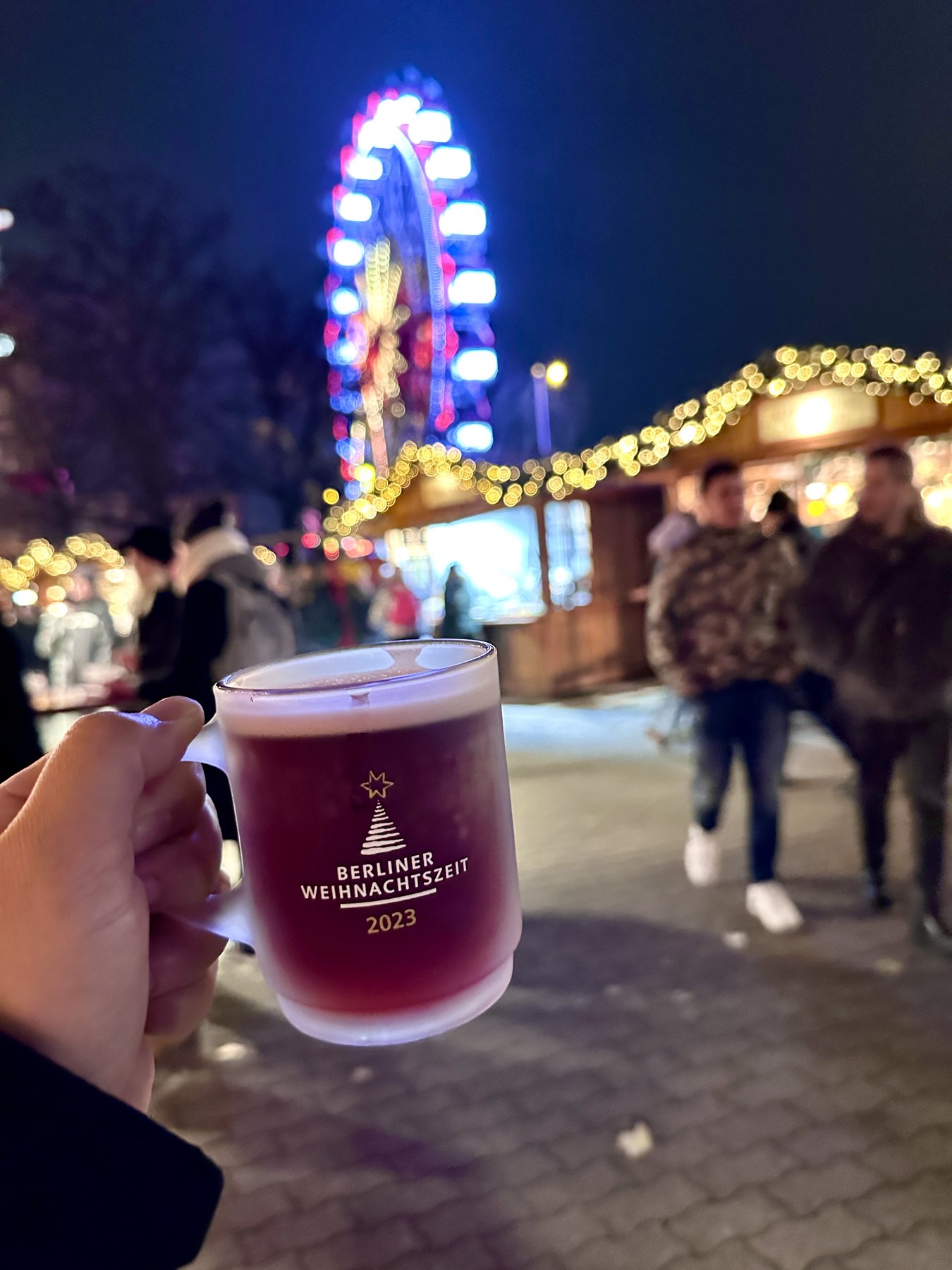 Glühwein mug at Berliner Weihnachtszeit Christmas market at Alexanderplatz, Ferris wheel glowing in the background