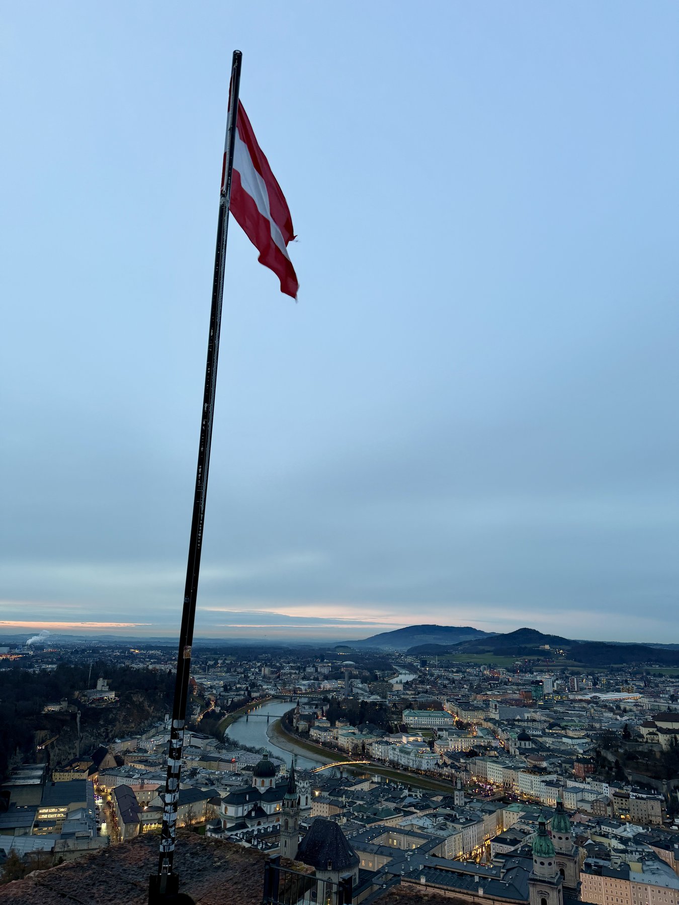 Austrian flag flying over Salzburg at blue hour from Hohensalzburg Fortress, city lights and the Salzach river below