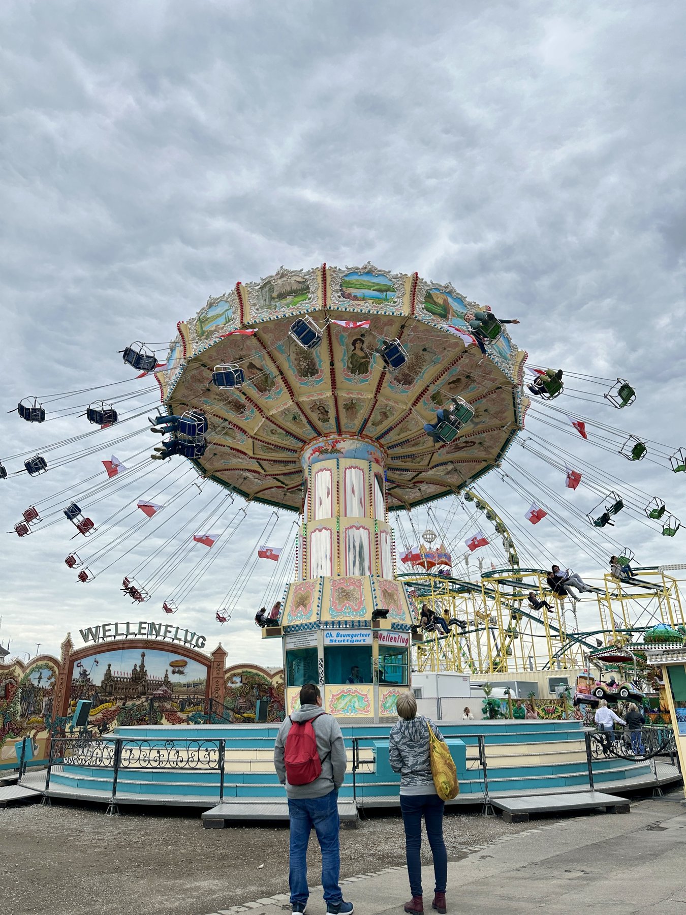 Wellenflug swing carousel in full spin at the Stuttgart Spring Festival, two people watching from below